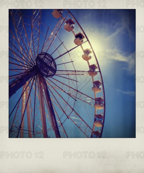Visitors admire the towering Ferris wheel as it stands against a vibrant blue sky. The sunlight gleams through the structure, creating a captivating atmosphere perfect for capturing memories