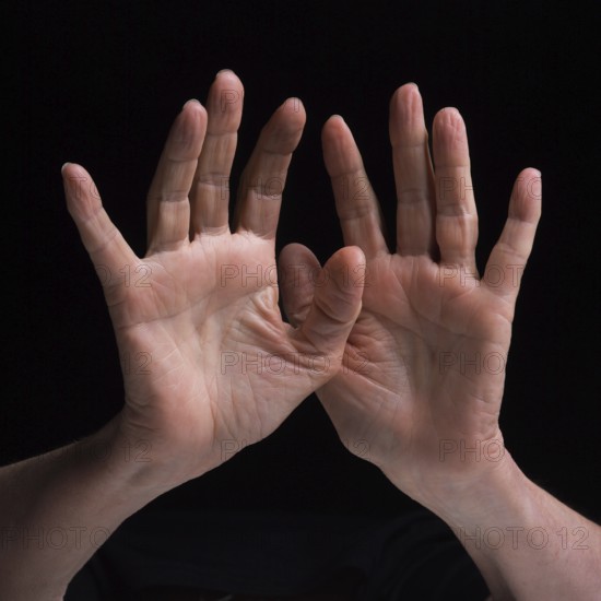 Two hands are raised and positioned in a distinctive gesture, highlighting their textures and details against a black background. The composition emphasizes human expression and art