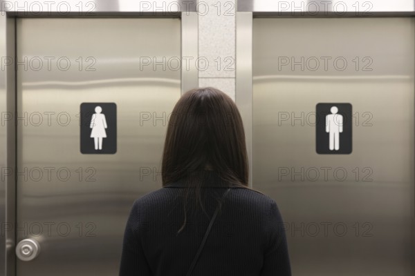 Woman in front of men's and women's bathroom doors. Concept of public restroom access and trans rights debate. Generative ai, AI generated