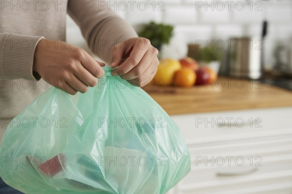Woman tying up a garbage bag in a home kitchen as part of daily waste disposal. Generative ai, AI generated