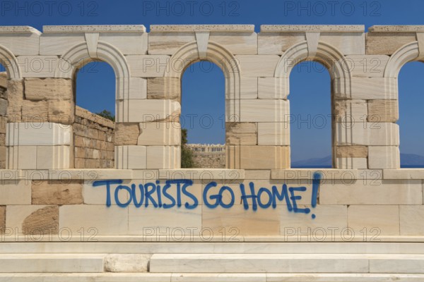 Blue graffiti reading Tourists go home on antique ruin wall with no people present. Generative ai, AI generated