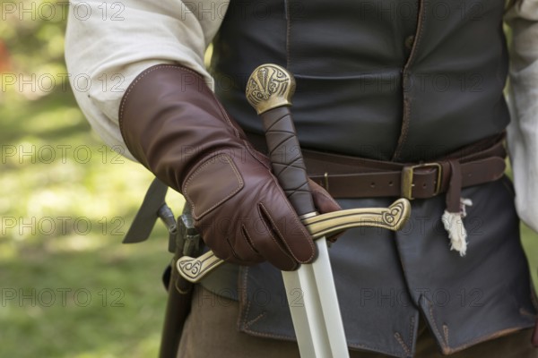 Hand in leather glove holding medieval sword hilt with gemstone. Concept of medieval or LARP cosplay authenticity. Generative ai, AI generated