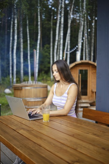 A woman finishes remote work while sitting on the terrace in the evening and is about to go to outdoor sauna