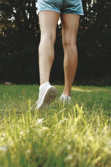 Close-up of female legs in sneakers walking on grass in the meadow
