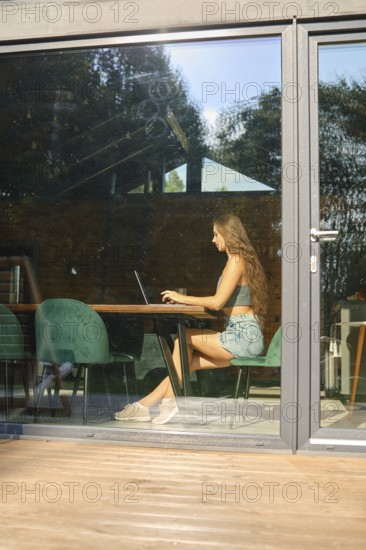 A view through the window of a woman blogger writing a post on her social network about her vacation experiences in a country house. Concept of local retreat