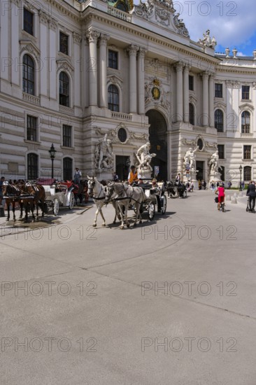 Everyday scene full of tourists and horse-drawn carriages on Michaelerplatz in front of the Michaelertrakt of the Vienna Hofburg Imperial Palace, Vienna, Austria, for editorial use only