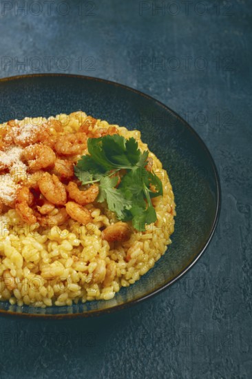 Risotto with shrimp, in a bowl, on a textured surface, with a side dish of fresh coriander, homemade, no people