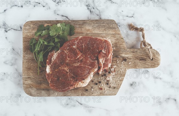 Raw pork steak, pork neck, on a chopping board, marble table, top view, with spices and coriander, no people