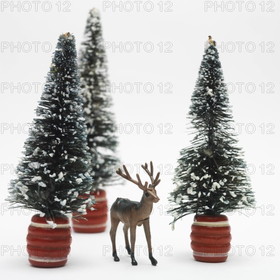 A detailed deer figurine stands in front of two snowy miniature trees, creating a festive atmosphere. This charming arrangement enhances holiday decorations and celebrations