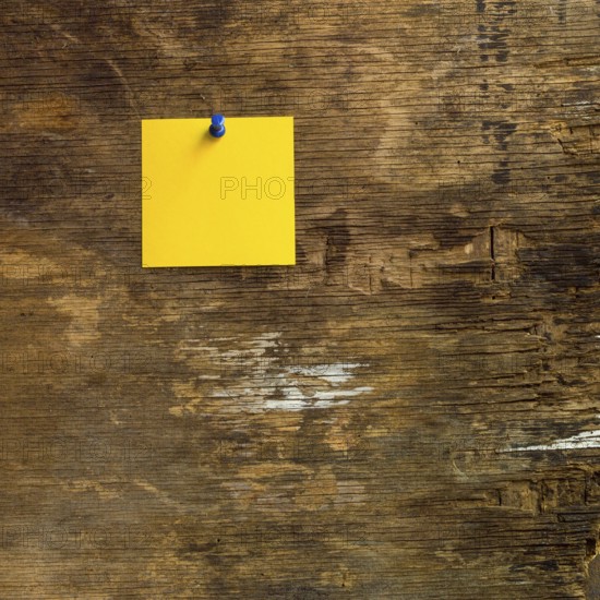 A vibrant yellow sticky note is tacked to a weathered wooden surface, showcasing its artistic charm. The bold color stands out against the textured rustic background