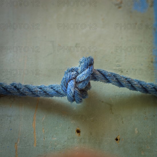 A close-up view reveals an intricately tied blue rope knot resting on a textured surface, highlighting the detailed craftsmanship involved in knot-making