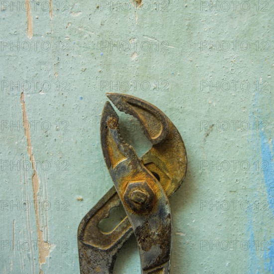 A pair of rusty pliers hangs on a worn blue wall, showcasing the wear and tear of years in a workshop setting filled with a sense of nostalgia and craftsmanship