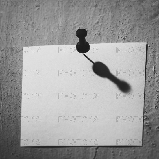 A blank piece of note paper is pinned to a textured wall, casting a compelling shadow that emphasizes shapes and contrast, highlighting simplicity and minimalism