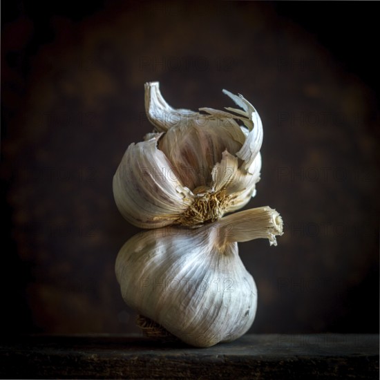 Garlic cloves are arranged carefully against a black background, emphasizing their natural texture and form. The lighting highlights the cloves' layers and contours, creating an artistic effect