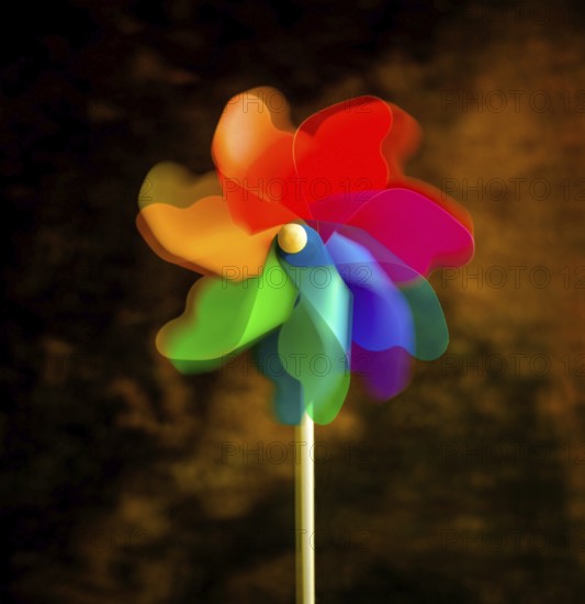 A bright pinwheel spins playfully, showcasing vibrant colors of red, blue, green, and orange. This cheerful toy brings excitement and delight in a simple outdoor setting