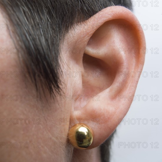 Detailed view of a woman's ear featuring a shiny drop earring. The focus is on the ear structure and the reflection from the earring, highlighting elegance and style