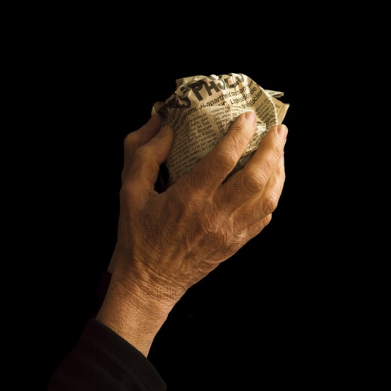 A hand gently grasps a crumpled newspaper, symbolizing the weight of information and how news is perceived. The dark background adds a sense of contemplation and nostalgia
