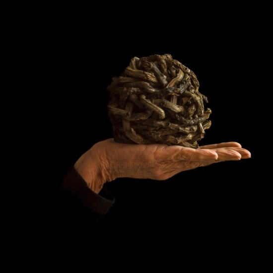 A hand supports a uniquely crafted ball made of intertwined materials, resting against a dark backdrop. The arrangement contrasts textures and highlights creativity in design