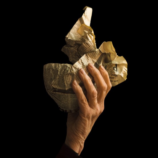 A hand grips a crumpled newspaper, illustrating a mix of emotions and memories. The dark background contrasts with the textured paper, evoking curiosity and introspection