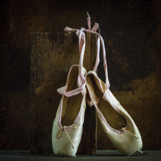 Delicate ballet shoes are placed on a wooden block, showcasing their soft texture and ribbons. The warm brown background enhances their classic beauty and significance in dance