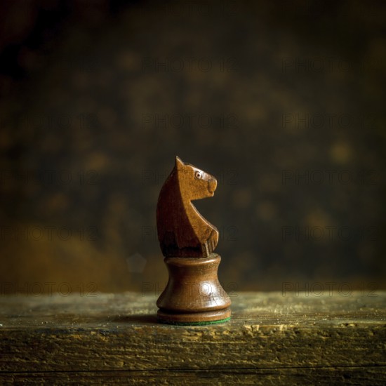 A beautifully crafted wooden chess knight piece stands prominently on a wooden surface. The backdrop is softly blurred, enhancing the warm, rustic ambiance, creating a focused view on the knight