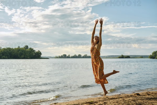 A carefree woman in a colourful sundress dances with joy along the riverbank on a sunny afternoon