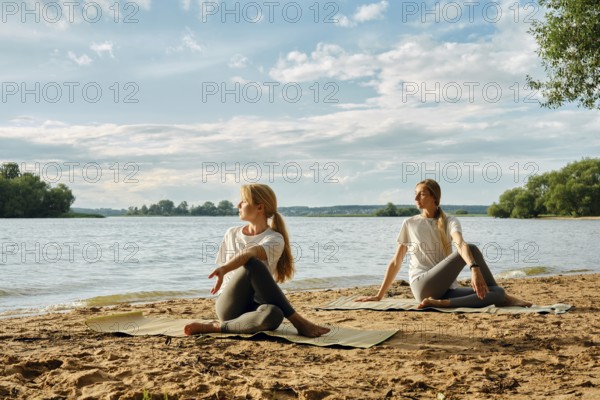 Two women practicing yoga on sandy shores by a river. Surrounded by trees and under a bright sky, they enjoy a peaceful afternoon, enhancing relaxation and mindfulness in nature