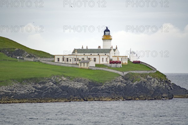 A lighthouse on a green coastal cliff next to the sea under a cloudy sky, Shetland Islands, Scotland, Great Britain