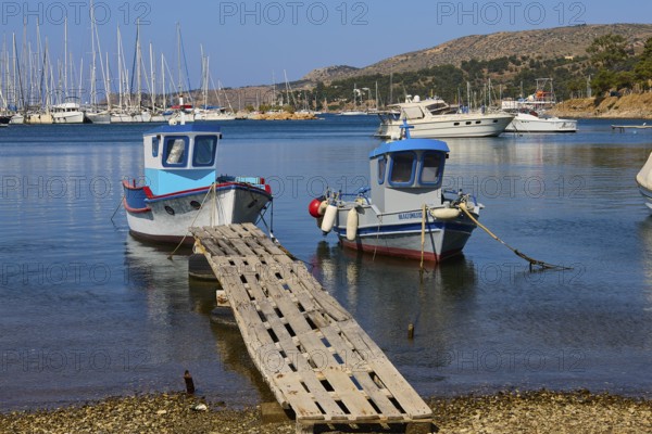 Two colourful boats on a wooden jetty with blue water and yachts in the background, Lakki, Leros, Dodecanese, Greek Islands, Greece