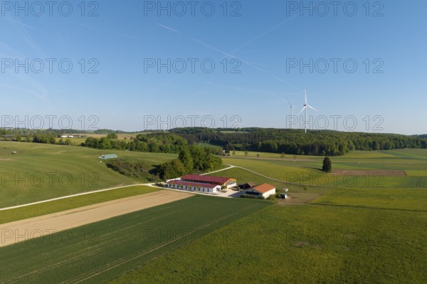 An expansive field landscape with a farm and wind turbines, under a clear blue sky, near Westerheim, Swabian Alb, Baden-Württemberg, Germany