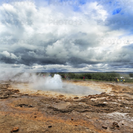 Steaming Strokkur with water column, tourists observe eruption, high temperature area Haukadalur, tourist attraction at the Golden Circle, dramatic cloudy sky, Sudurland, Iceland