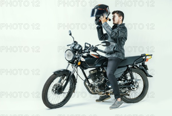 Man on motorcycle putting on helmet, isolated background. Young motorcyclist wearing safety helmet. Motorcycle safety concept