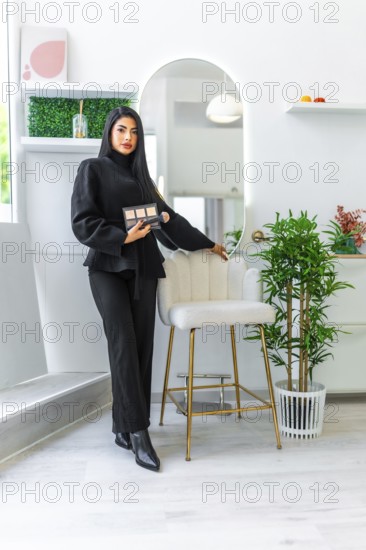Beautician posing with makeup palette in modern beauty salon, showcasing her expertise and the salon's aesthetic
