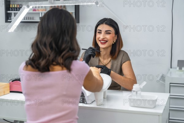 Smiling manicurist applying nail polish to her customer in a beauty salon, performing a professional manicure