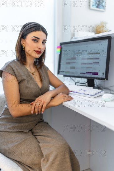 Beautician sitting at desk, using computer software for managing appointments in a modern and bright beauty salon