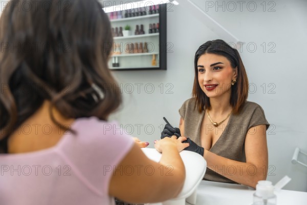 Smiling nail technician performing manicure on customer's fingernails, applying nail polish in a beauty salon