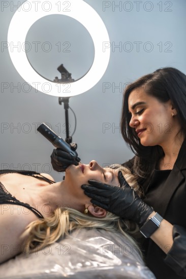 Beautician performing a lip blushing treatment using a rotary tattoo pen in a modern aesthetic center