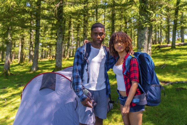 Young couple of hikers embracing and smiling next to their tent in a lush forest, enjoying a joyful camping trip together