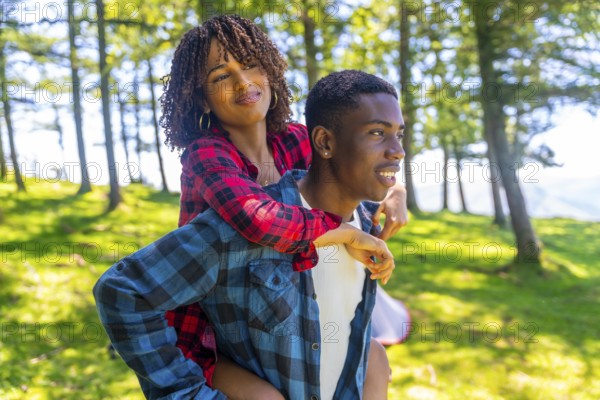 Young man giving piggyback ride to his girlfriend in forest during camping trip, enjoying summer vacation in nature