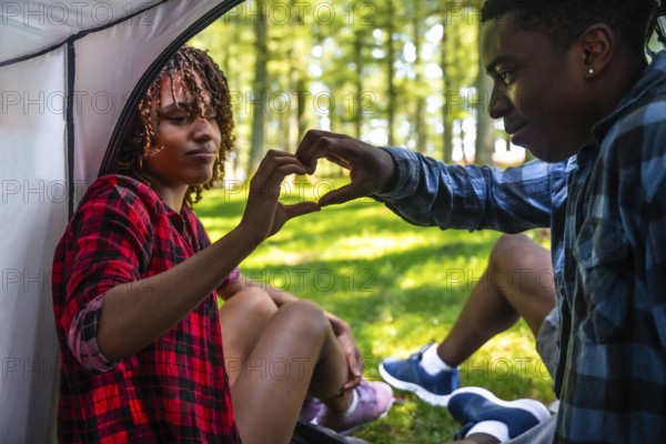 Young campers making heart shape with hands while sitting in tent during camping trip in forest