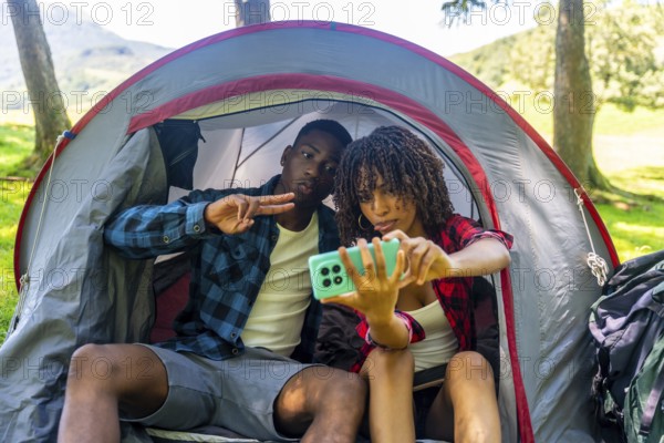 Two young campers are taking a selfie inside their tent, enjoying a fun camping trip in nature