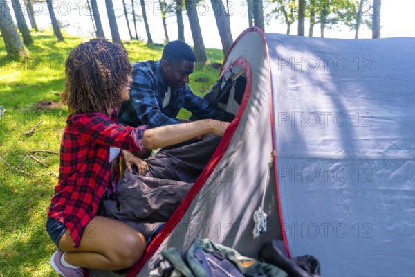 Hikers are setting up camp in the forest, putting sleeping bags inside their tent on a beautiful sunny day