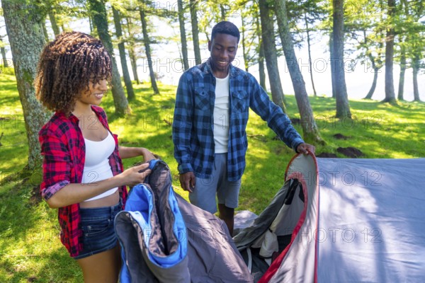 Young black couple setting up their tent in a forest campground near a lake, enjoying a summer camping trip