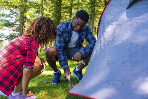 Young black couple setting up their tent in a serene forest, embracing the joy of camping and connecting with nature on a sunny day