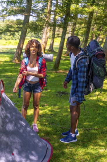 Young couple setting up their campsite while enjoying a backpacking adventure in the lush woods, surrounded by vibrant greenery and nature