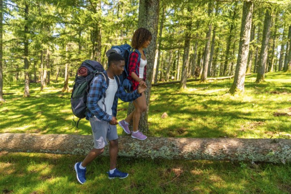 Young backpacking couple carefully balancing on a fallen tree trunk while hiking through a lush green forest