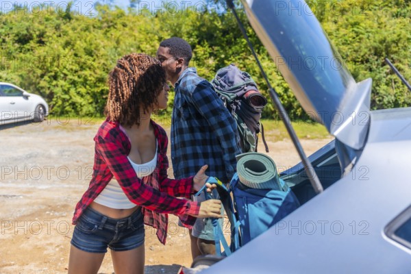 Young couple unpacking their backpacks from the trunk of the car, excitedly preparing for an adventurous hiking trip in the beautiful outdoors