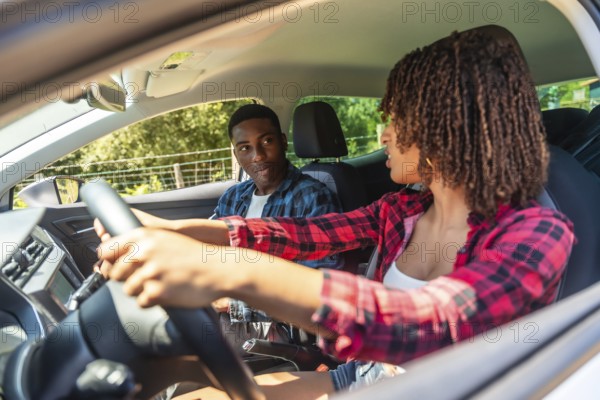 Young woman learning to drive, receiving guidance from her instructor as they navigate the car on a sunny day in the countryside