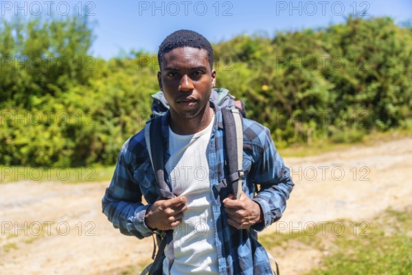 Confident young hiker wearing a backpack, enjoying a sunny day while discovering a beautiful nature trail surrounded by lush greenery