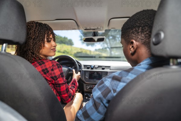 Young black couple driving a modern car on a sunny day, laughing and enjoying every moment of their exciting road trip adventure